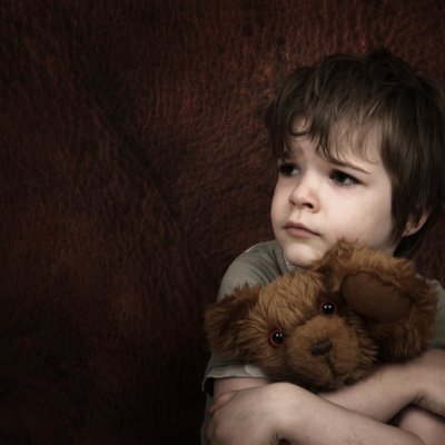 Young child looking distressed and holding teddy bear. 